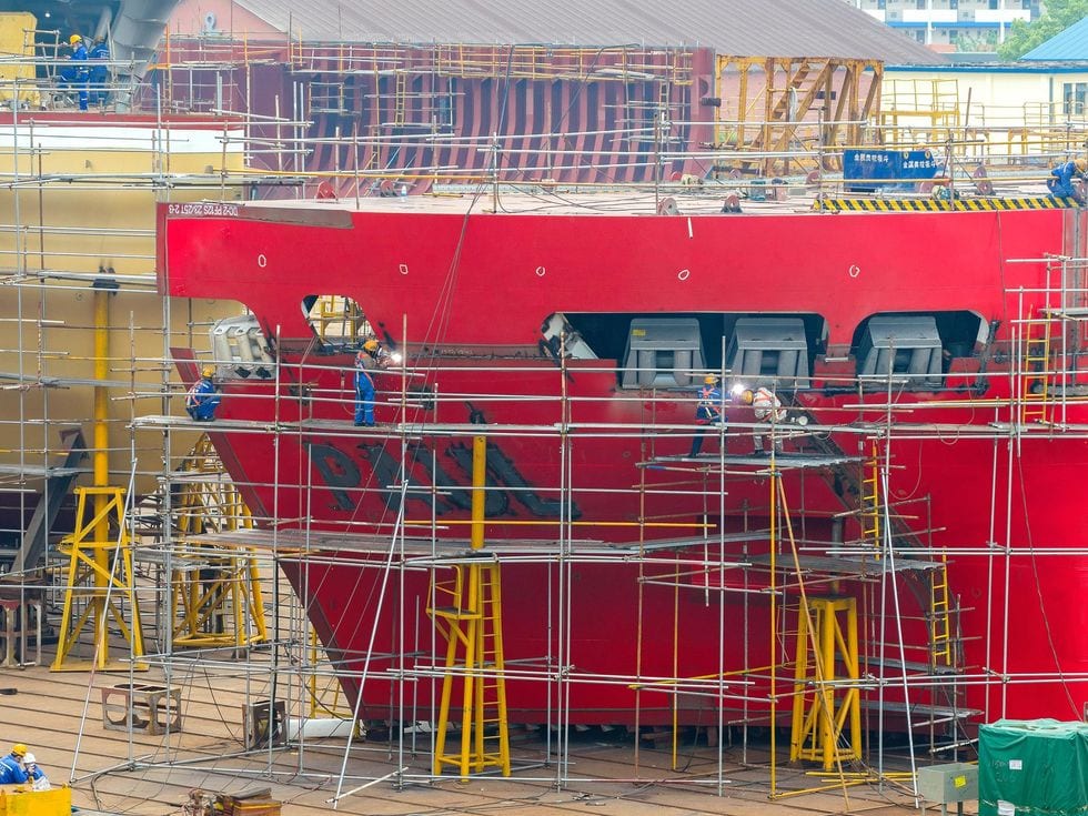 Several workers on scaffolding as they weld a large vessel in an industrial shipyard.