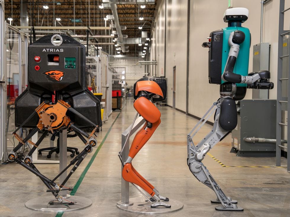 Three bipedal robots lined up in a warehouse, showing their evolving designs.