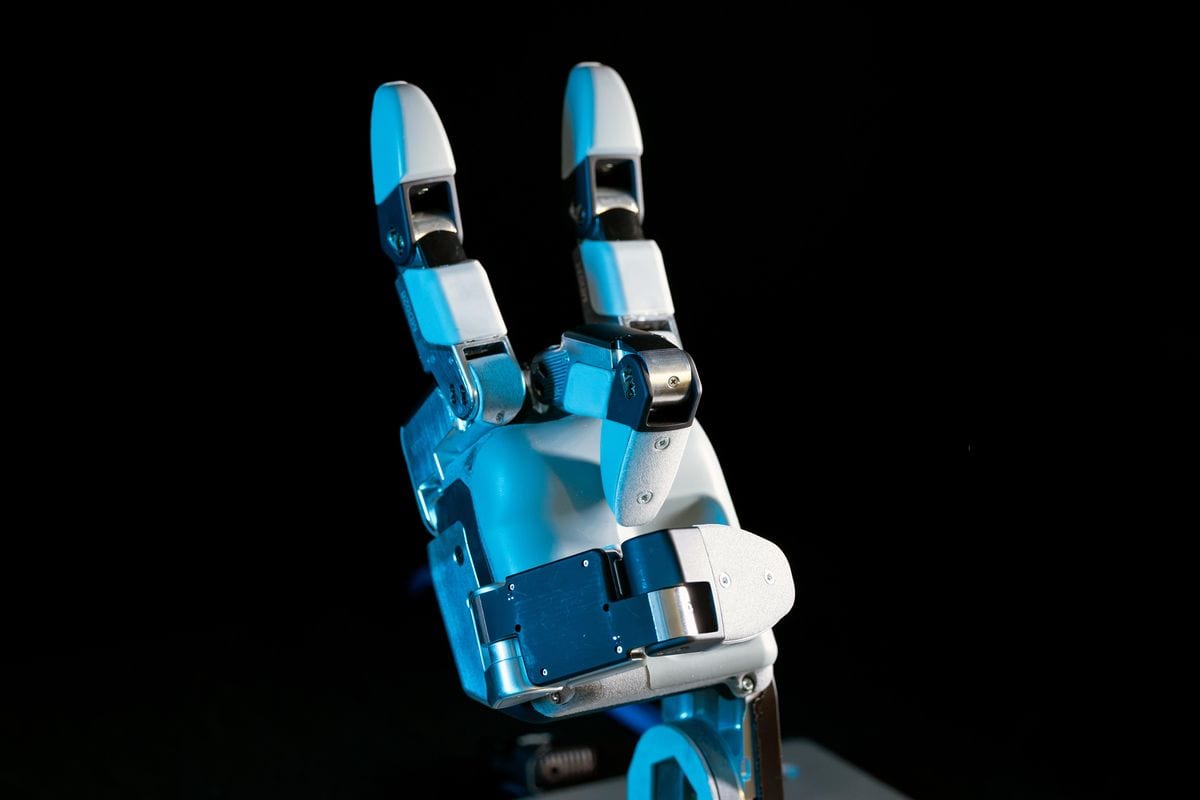 Close-up of a robotic hand with three fingers and a thumb, making a gesture similar to the “sign of the horns”.