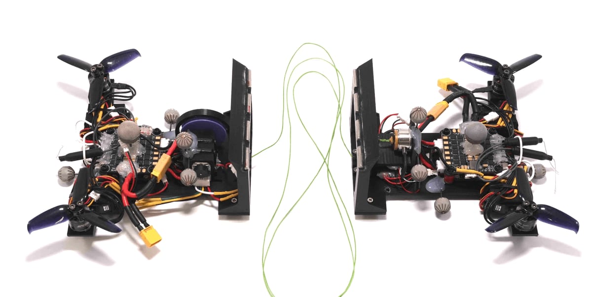 Two small dual-propeller robots facing each other, connected by a loose green cord