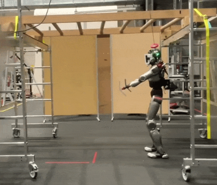 Humanoid robot moves across scaffolding rigged as playground monkey bars in a lab while trying to keep its balance.