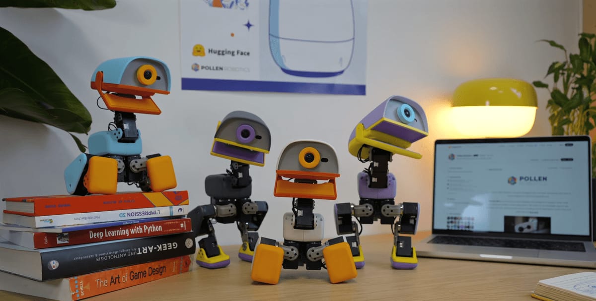 Colorful desk robots posed among books beside an open laptop in an office.
