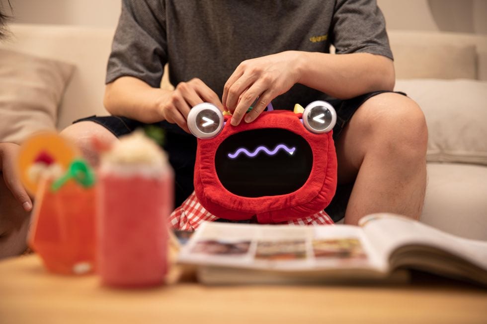 Person playing with a red plush robot toy that has a glowing digital face and eyes
