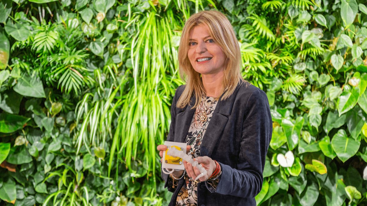 photo of a woman standing in front of greenery, holding a device shaped like a small octopus arm