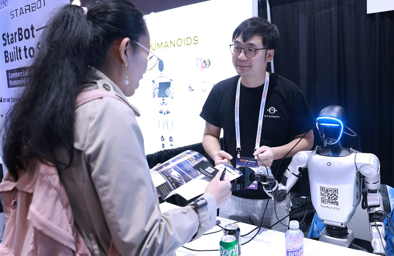A woman talking to a man and a humanoid robot at RoboBusiness 2025.