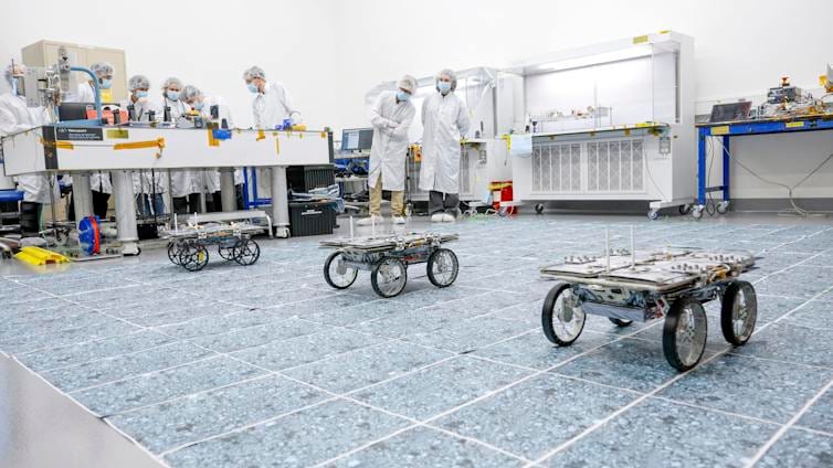 Three small robotic rovers drive across a sterile warehouse floor.